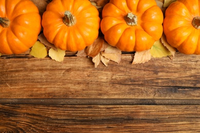 Flat lay composition with pumpkins and autumn leaves on wooden table. Space for text