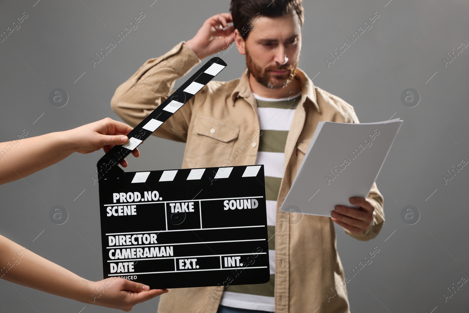 Photo of Actor performing while second assistant camera holding clapperboard on grey background, closeup