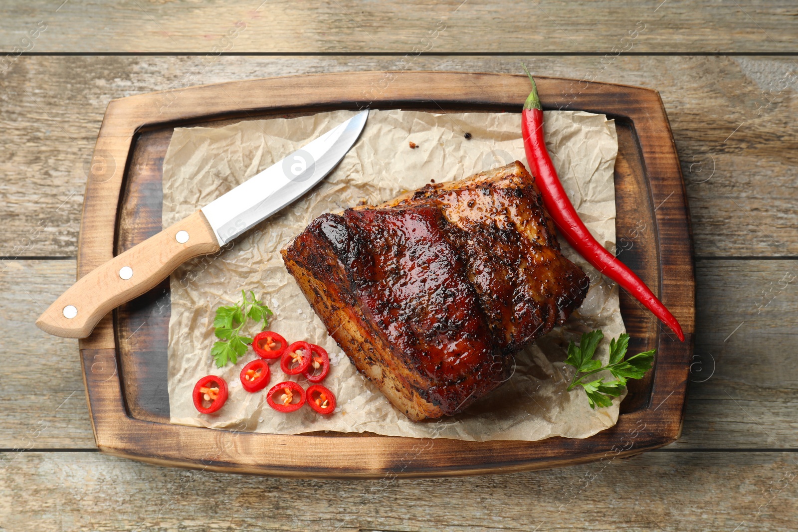 Photo of Piece of baked pork belly served with sauce and chili pepper on wooden table, top view