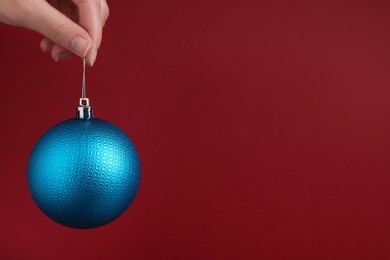 Photo of Woman holding blue Christmas ball on red background, closeup. Space for text