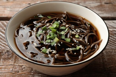 Photo of Tasty soup with buckwheat noodles (soba), onion and sesame in bowl on wooden table, closeup