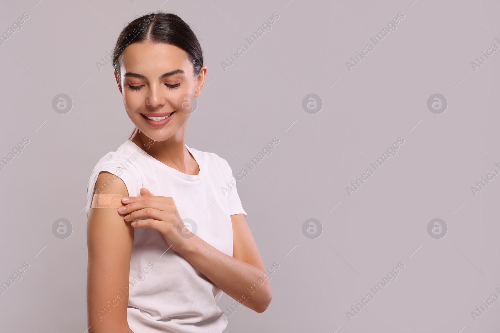 Photo of Woman with sticking plaster on arm after vaccination against light grey background, space for text