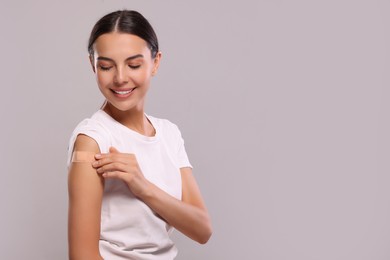 Woman with sticking plaster on arm after vaccination against light grey background, space for text