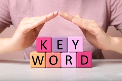 Woman demonstrating colorful cubes with word KEYWORD at grey marble table, closeup