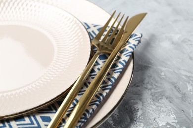 Photo of Clean plates, cutlery and napkin on light grey textured table, closeup