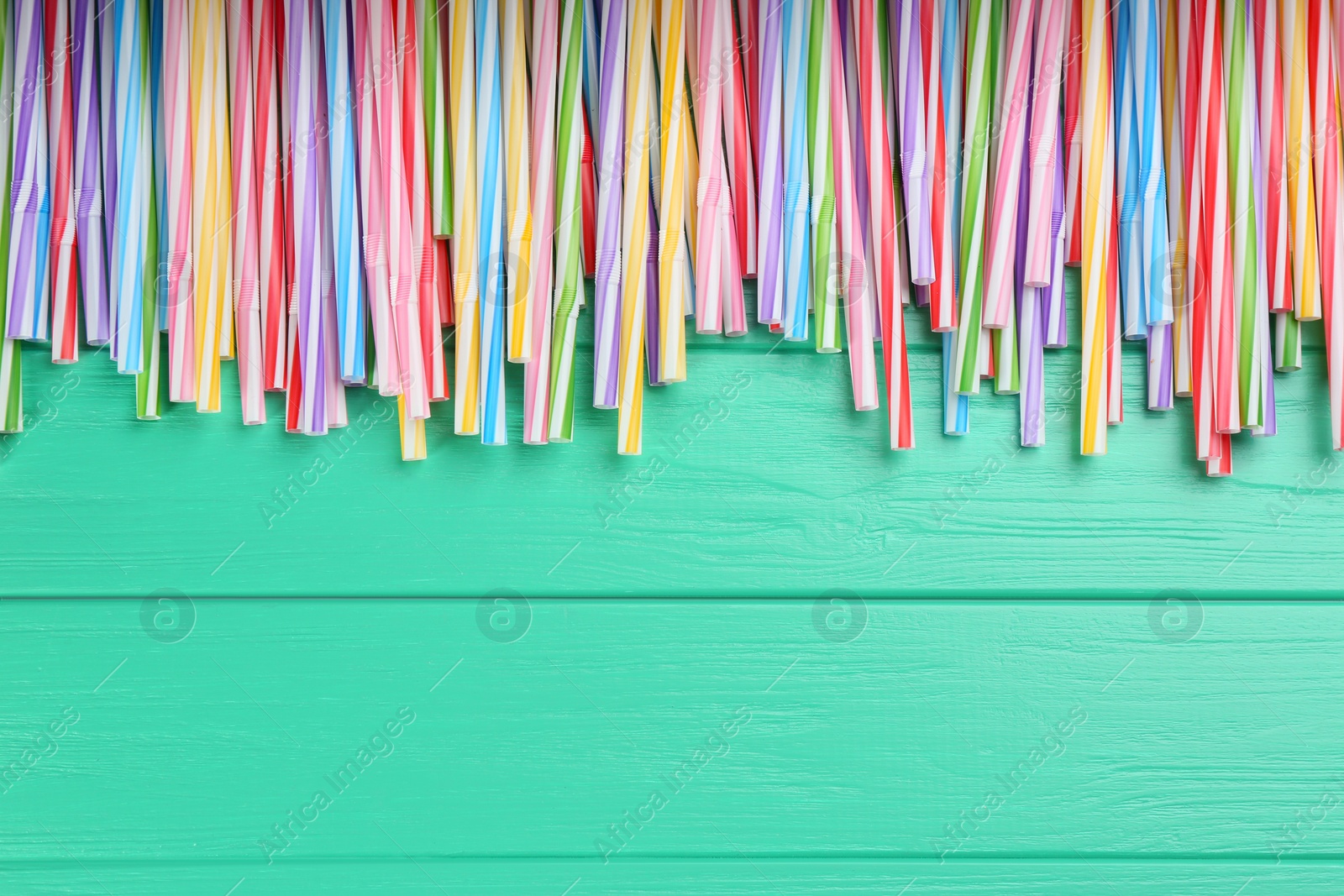Photo of Colorful plastic drinking straws on turquoise wooden table, flat lay. Space for text