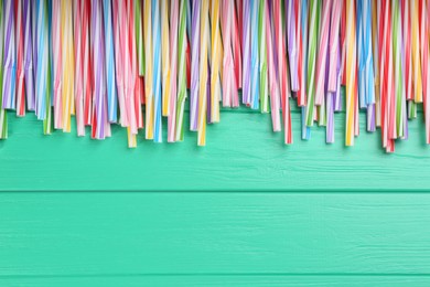 Colorful plastic drinking straws on turquoise wooden table, flat lay. Space for text