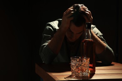 Photo of Addicted man and alcoholic drink at wooden table against black background, focus on glass