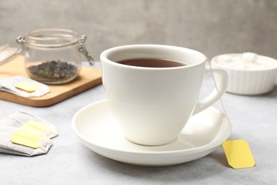 Photo of Tea brewing. Cup with hot drink and tea bags on light table, closeup