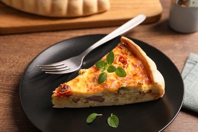 Photo of Delicious homemade vegetable quiche, oregano and fork on wooden table
