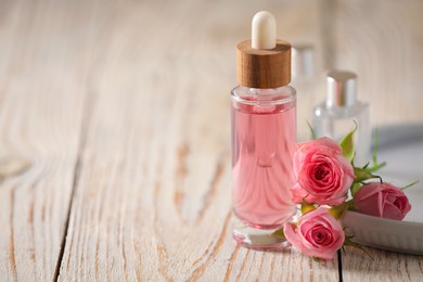 Bottle of essential rose oil and flowers on white wooden table, space for text