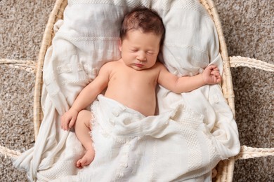 Cute newborn baby sleeping on white blanket in wicker crib, top view