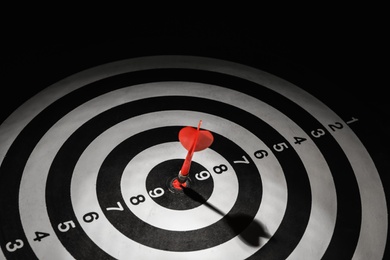 Photo of Red arrow hitting target on dart board against black background