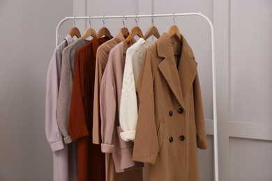 Rack with different stylish clothes near grey wall indoors