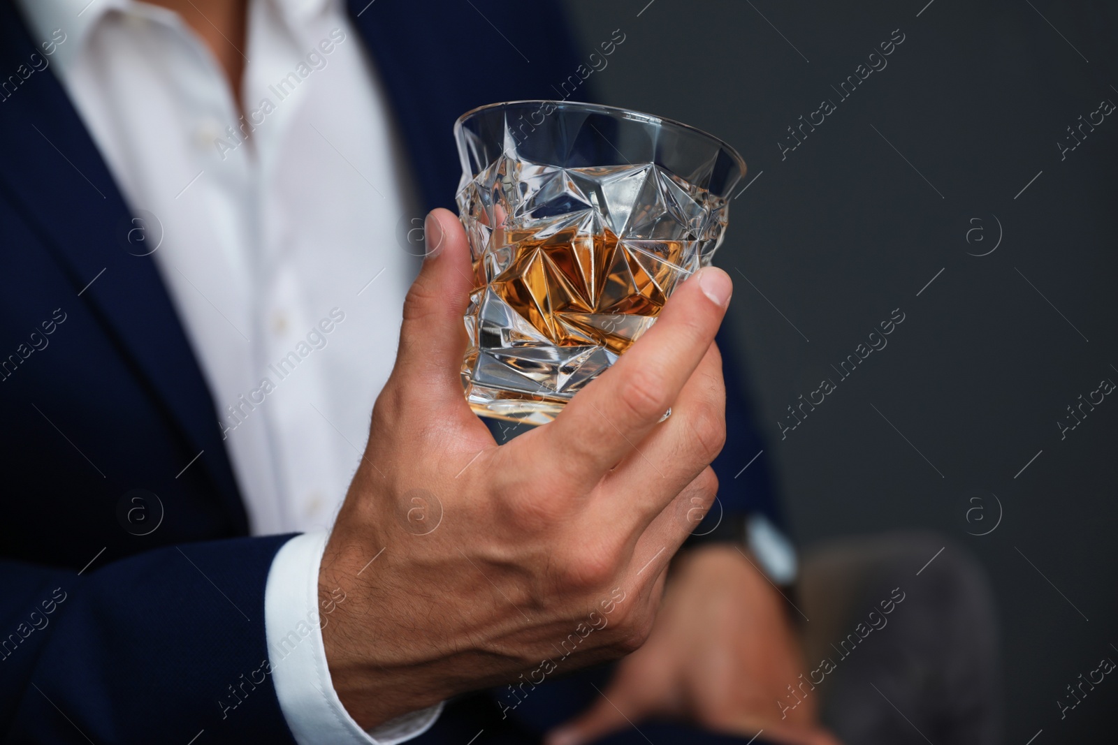 Photo of Young man with glass of whiskey on dark background, closeup view
