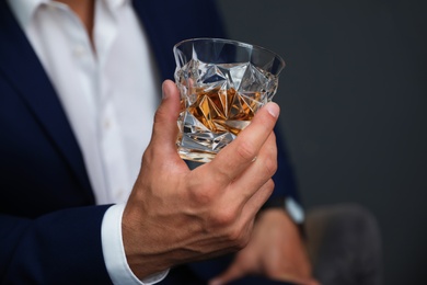 Young man with glass of whiskey on dark background, closeup view