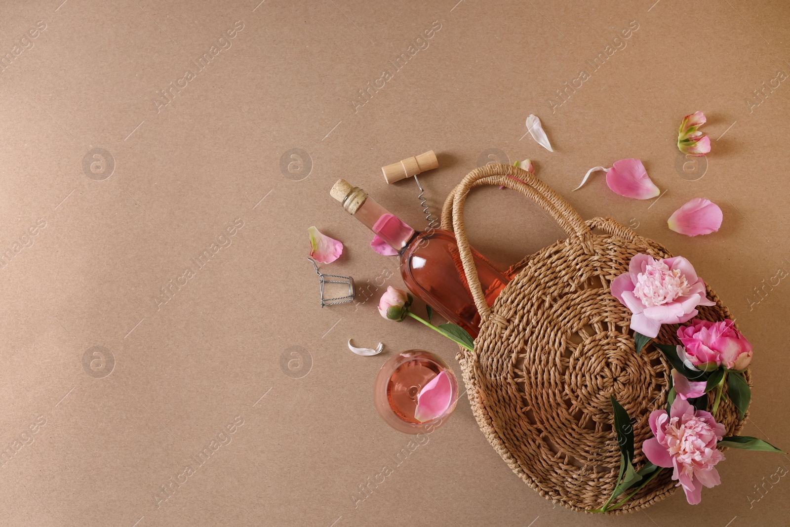 Photo of Flat lay composition with rose wine, wicker bag and beautiful pink peonies on brown background. Space for text