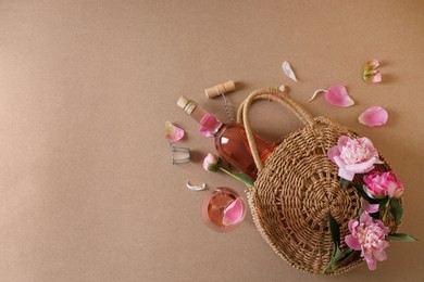 Flat lay composition with rose wine, wicker bag and beautiful pink peonies on brown background. Space for text