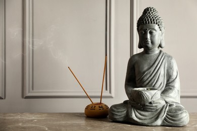 Photo of Buddha statue and incense sticks on grey table. Space for text