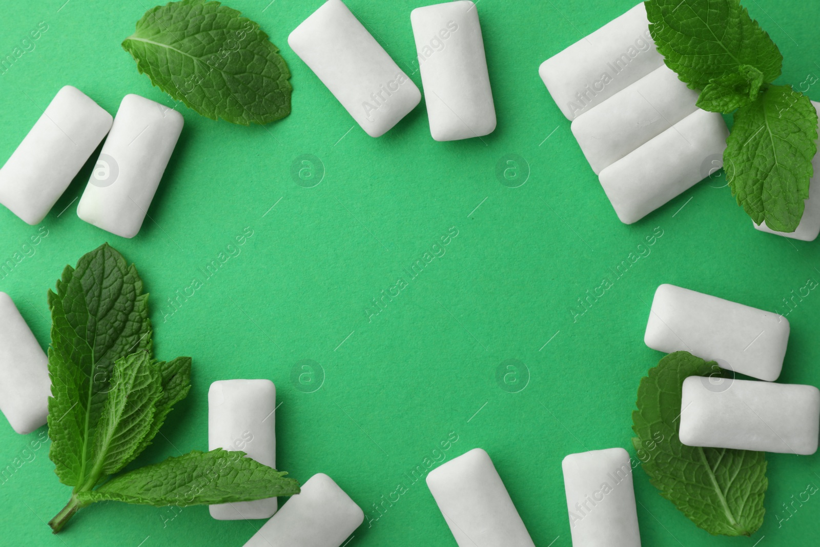 Photo of Frame made of tasty white chewing gums and mint leaves on green background, flat lay. Space for text