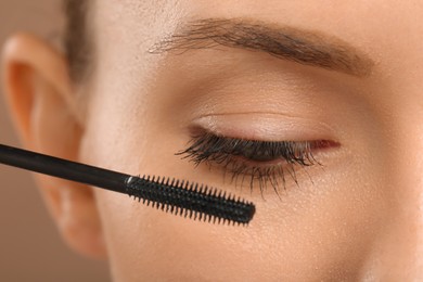 Photo of Woman applying mascara onto eyelashes against light brown background, closeup