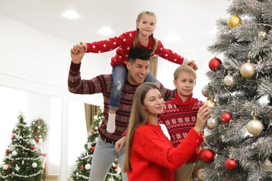 Mother and son decorating Christmas tree while father playing with daughter at home