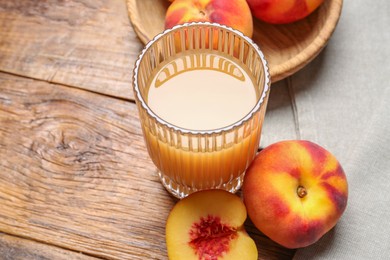 Photo of Glass of peach juice and fresh fruits on wooden table, closeup
