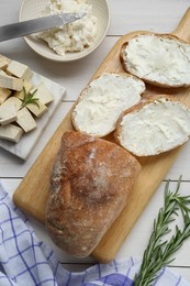 Photo of Slices of baguette with tofu cream cheese and rosemary on white wooden table, flat lay