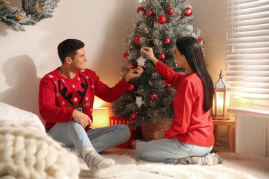 Happy couple decorating Christmas tree in bedroom