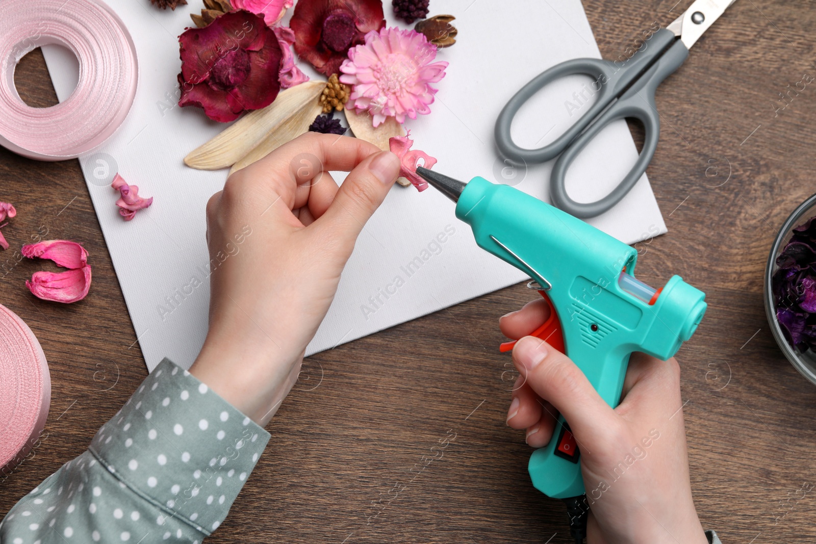 Photo of Woman using hot glue gun to make craft at wooden table, top view