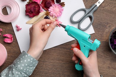 Woman using hot glue gun to make craft at wooden table, top view