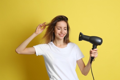 Beautiful young woman using hair dryer on yellow background