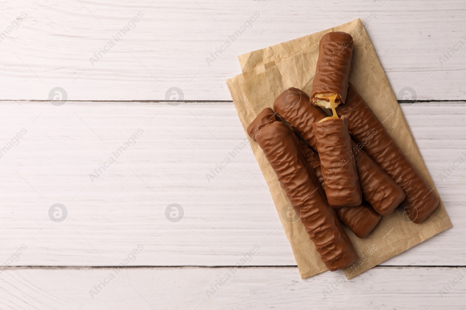 Photo of Tasty chocolate bars with caramel on white wooden table, top view. Space for text