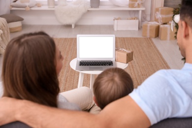 Photo of Family with child using video chat on laptop in room decorated for Christmas, back view