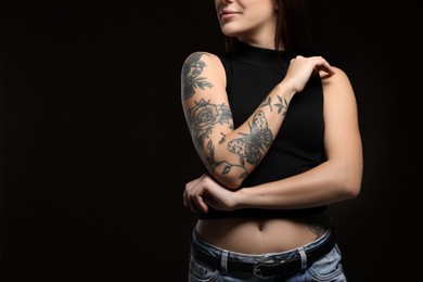 Photo of Beautiful woman with tattoos on arm against black background, closeup. Space for text