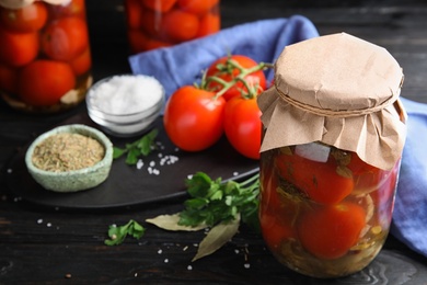 Photo of Pickled tomatoes in glass jars and products on black wooden table
