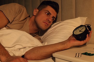 Man suffering from insomnia looking at time on alarm clock in bed indoors