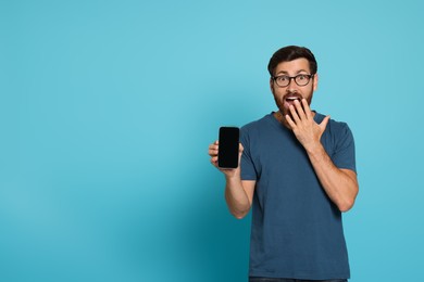 Emotional man with smartphone on light blue background. Space for text