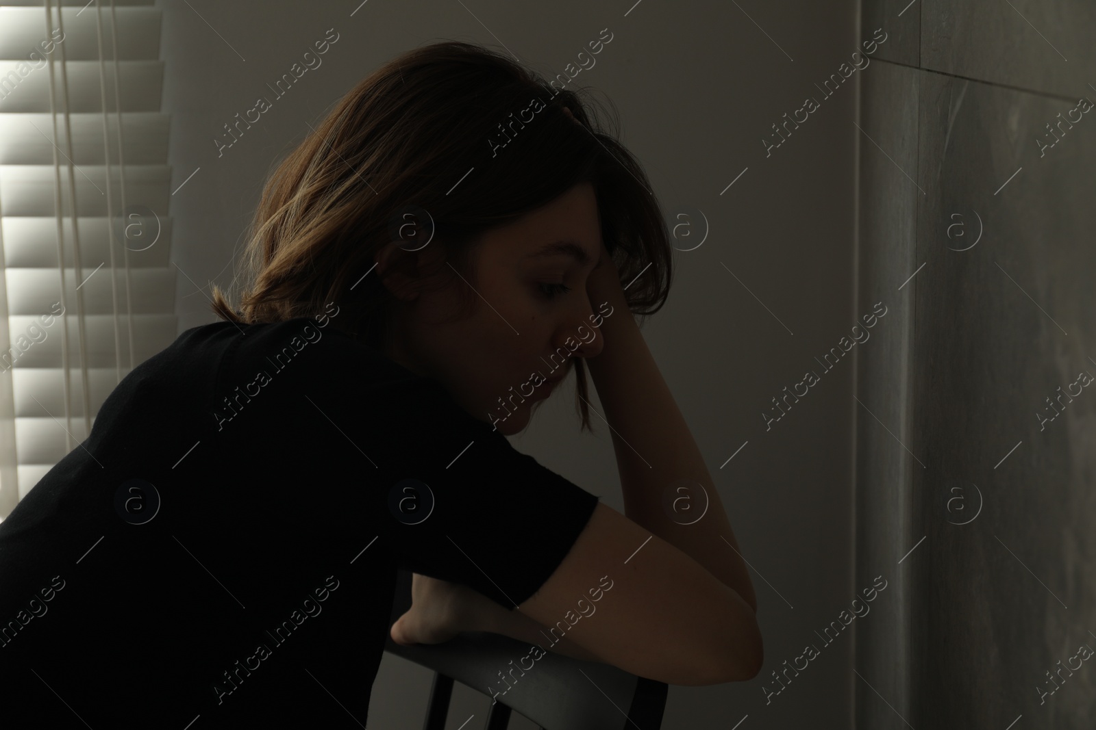 Photo of Sad young woman sitting on chair indoors, space for text