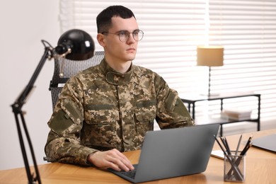 Photo of Military service. Young soldier working with laptop at wooden table in office