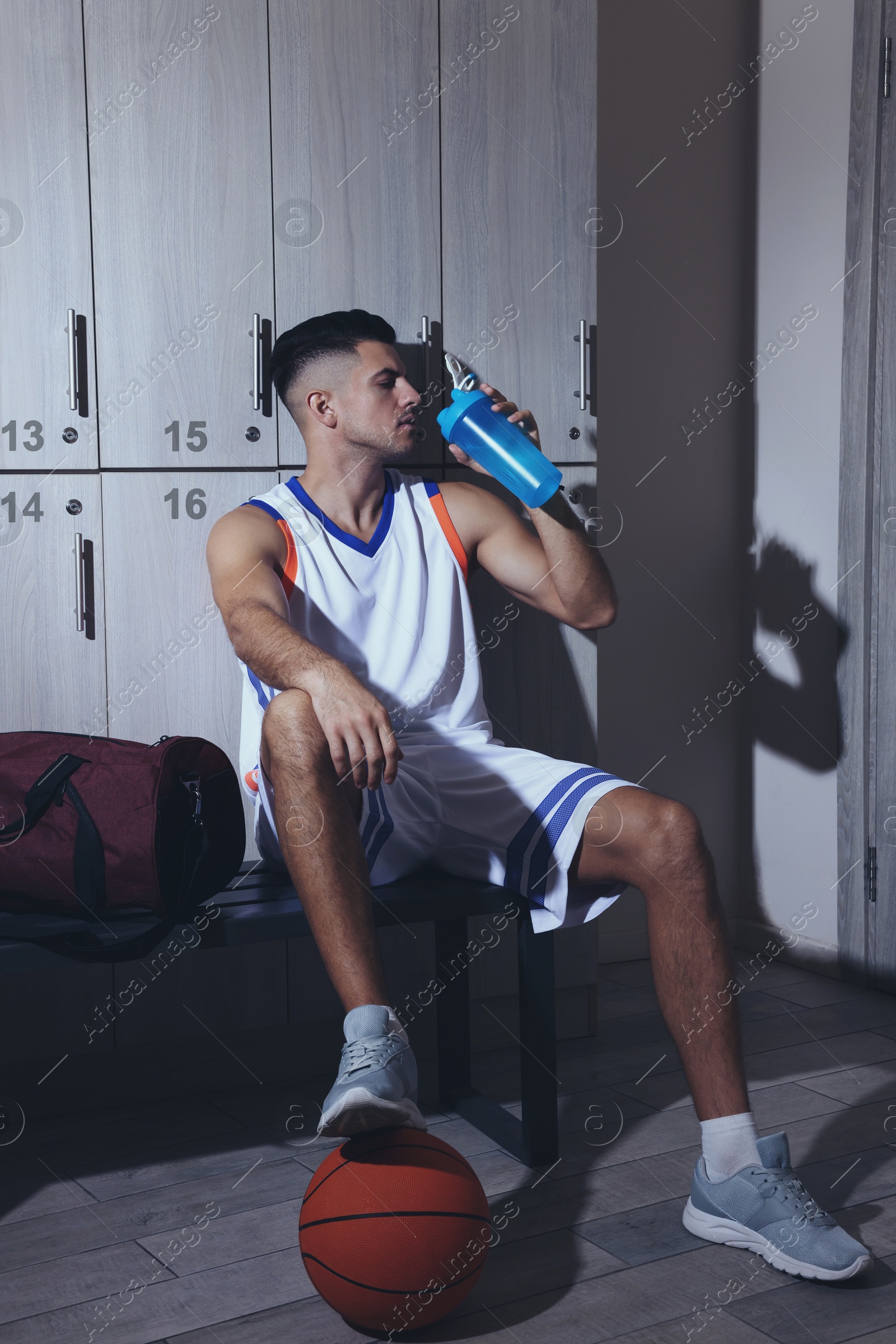 Image of Handsome man drinking water in locker room