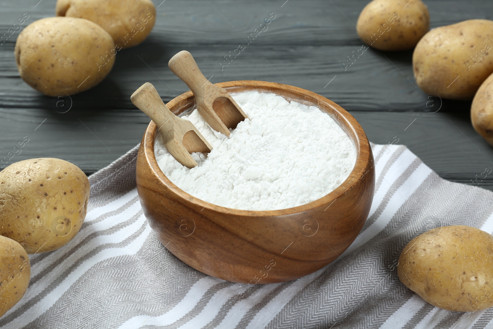 Photo of Bowl with starch, scoops and fresh potatoes on grey wooden table