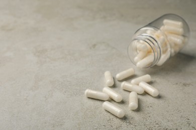 Overturned bottle with dietary supplement capsules on light grey table. Space for text