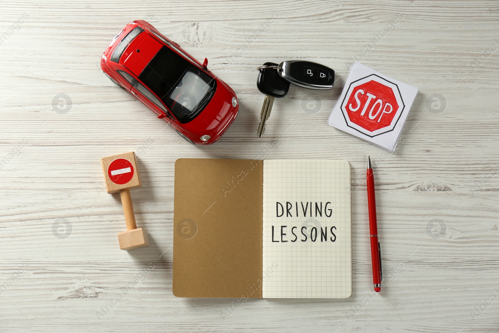 Photo of Flat lay composition with workbook for driving lessons and road signs on white wooden background. Passing license exam