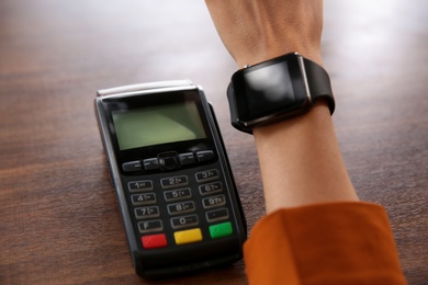 Photo of Woman making payment with smart watch at table, closeup