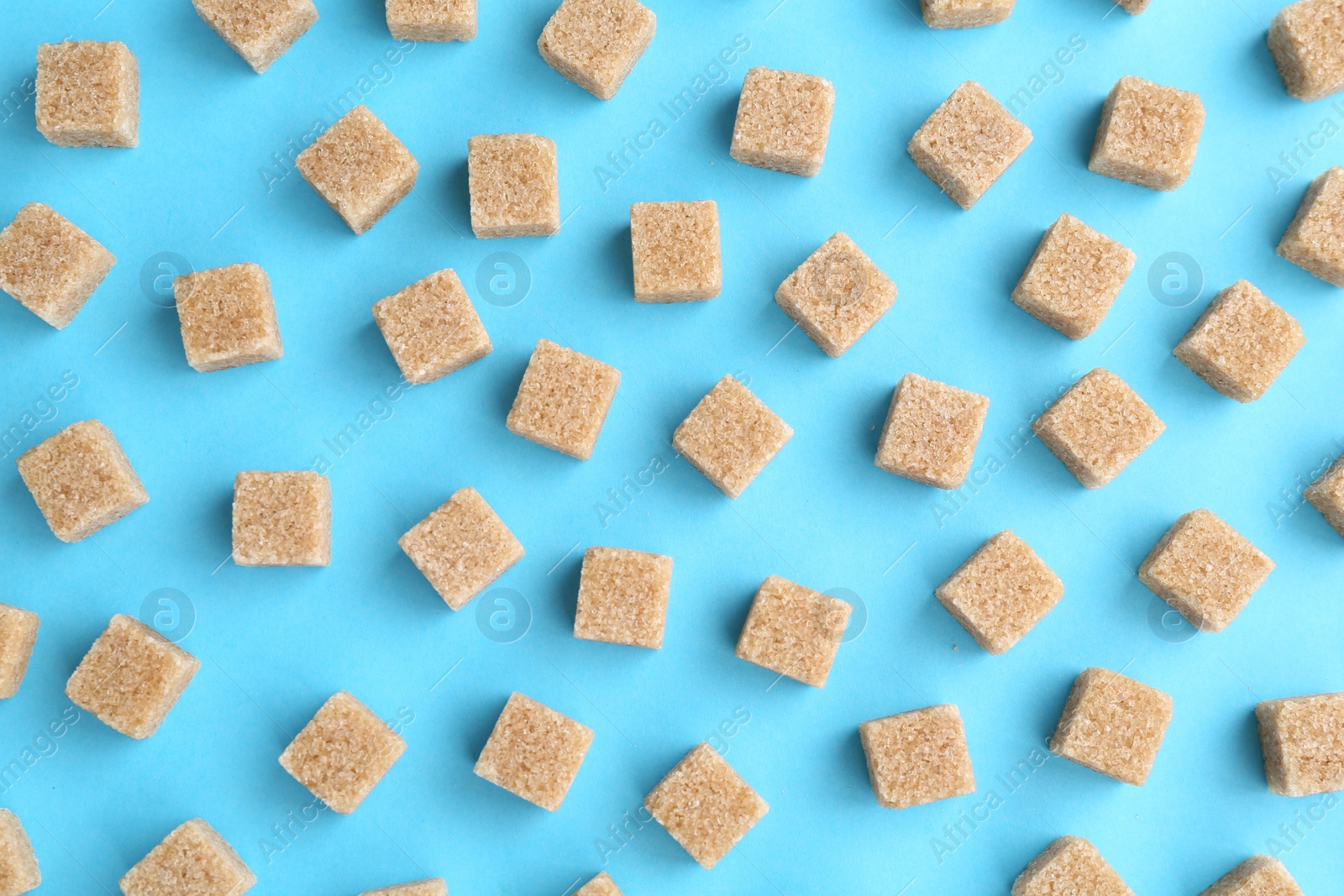 Photo of Brown sugar cubes on light blue background, top view