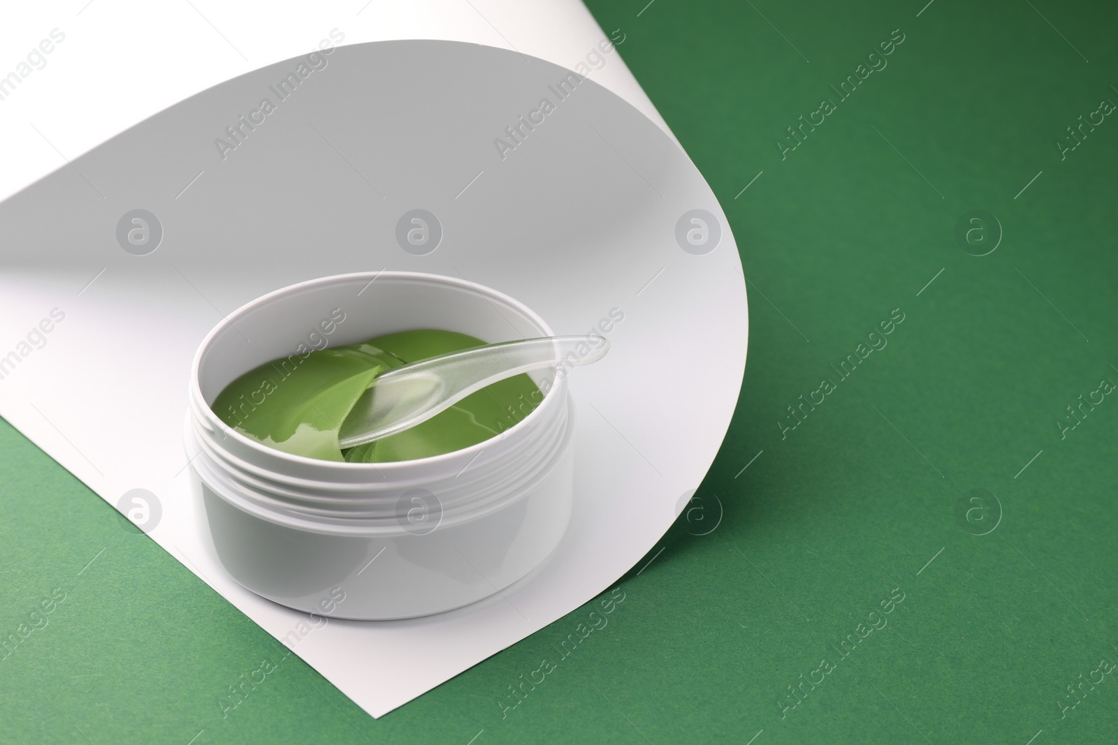 Photo of Jar of under eye patches with spoon on color background, space for text. Cosmetic product