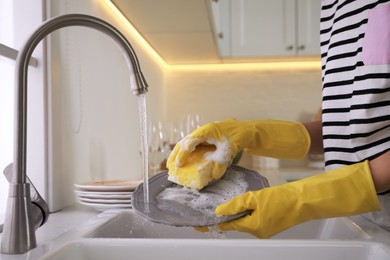 Woman washing plate above sink in kitchen, closeup