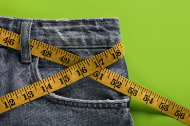 Photo of Jeans with measuring tape on green background, top view. Weight loss concept