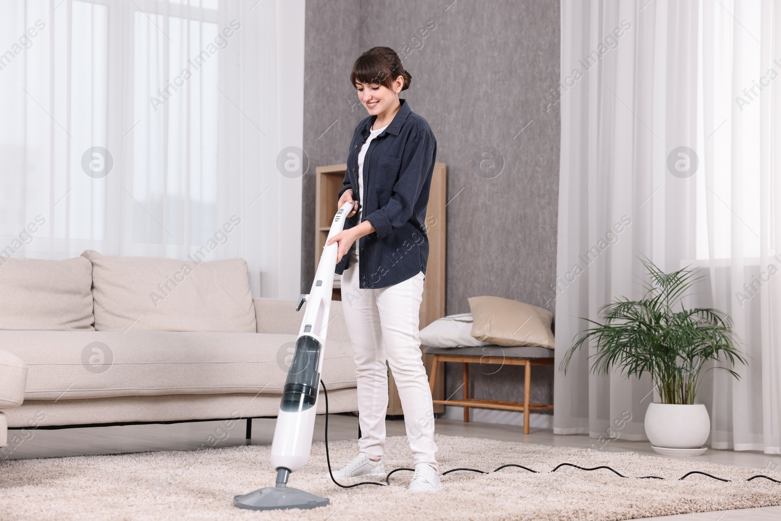 Photo of Happy young housewife vacuuming carpet at home